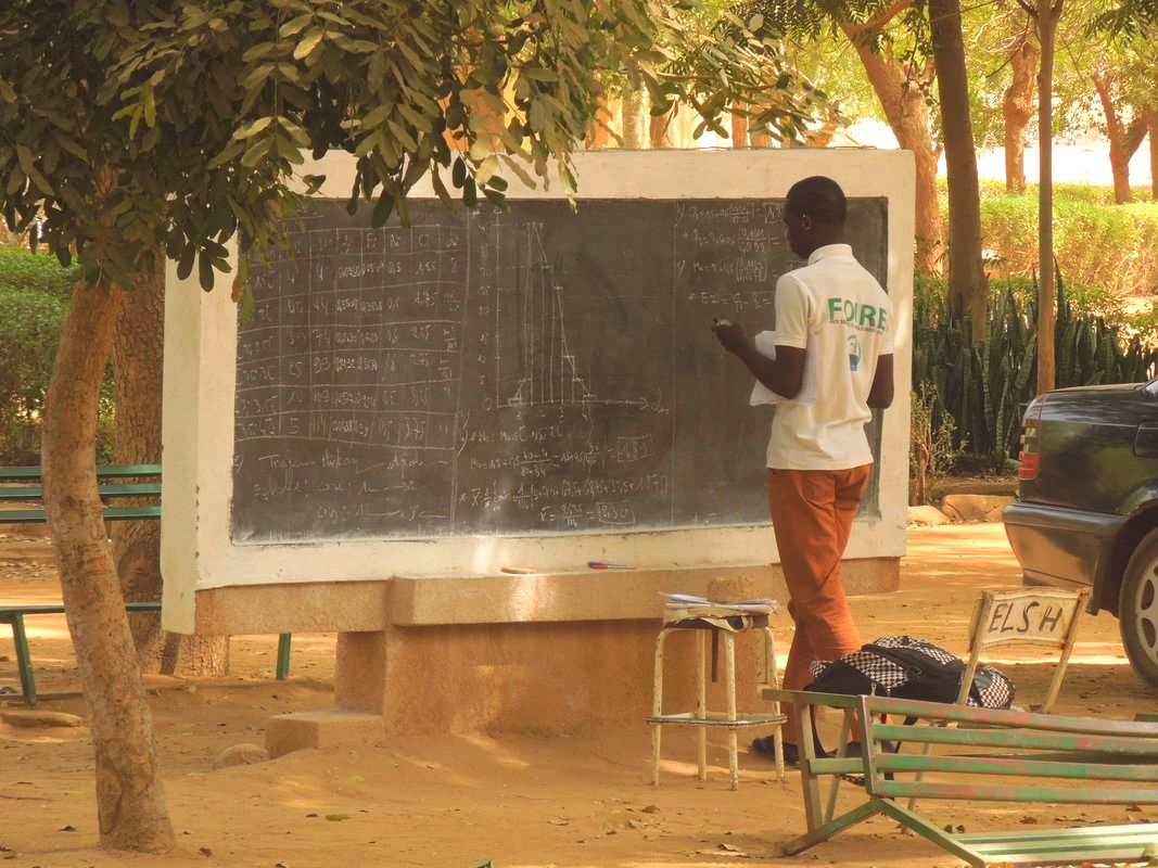 A student in the Social Sciences at Abdou Moumouni University doing homework problems on one of several outdoor chalkboards.